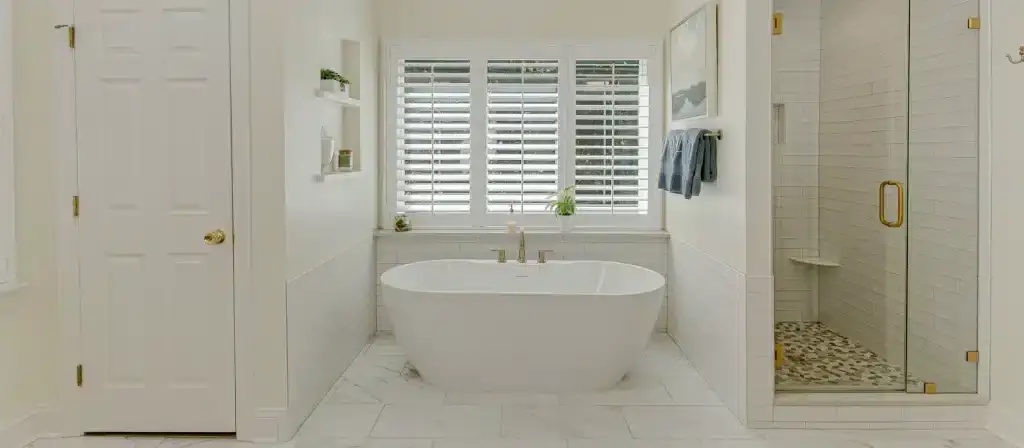 Elegant white bathroom featuring stylish plantation shutters on the window for privacy and light con.