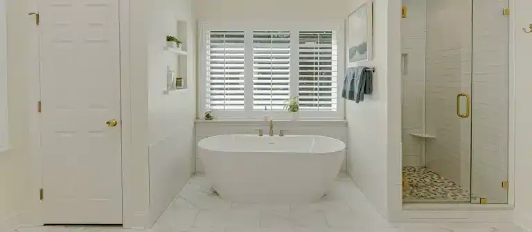Elegant white bathroom featuring stylish plantation shutters on the window for privacy and light con.